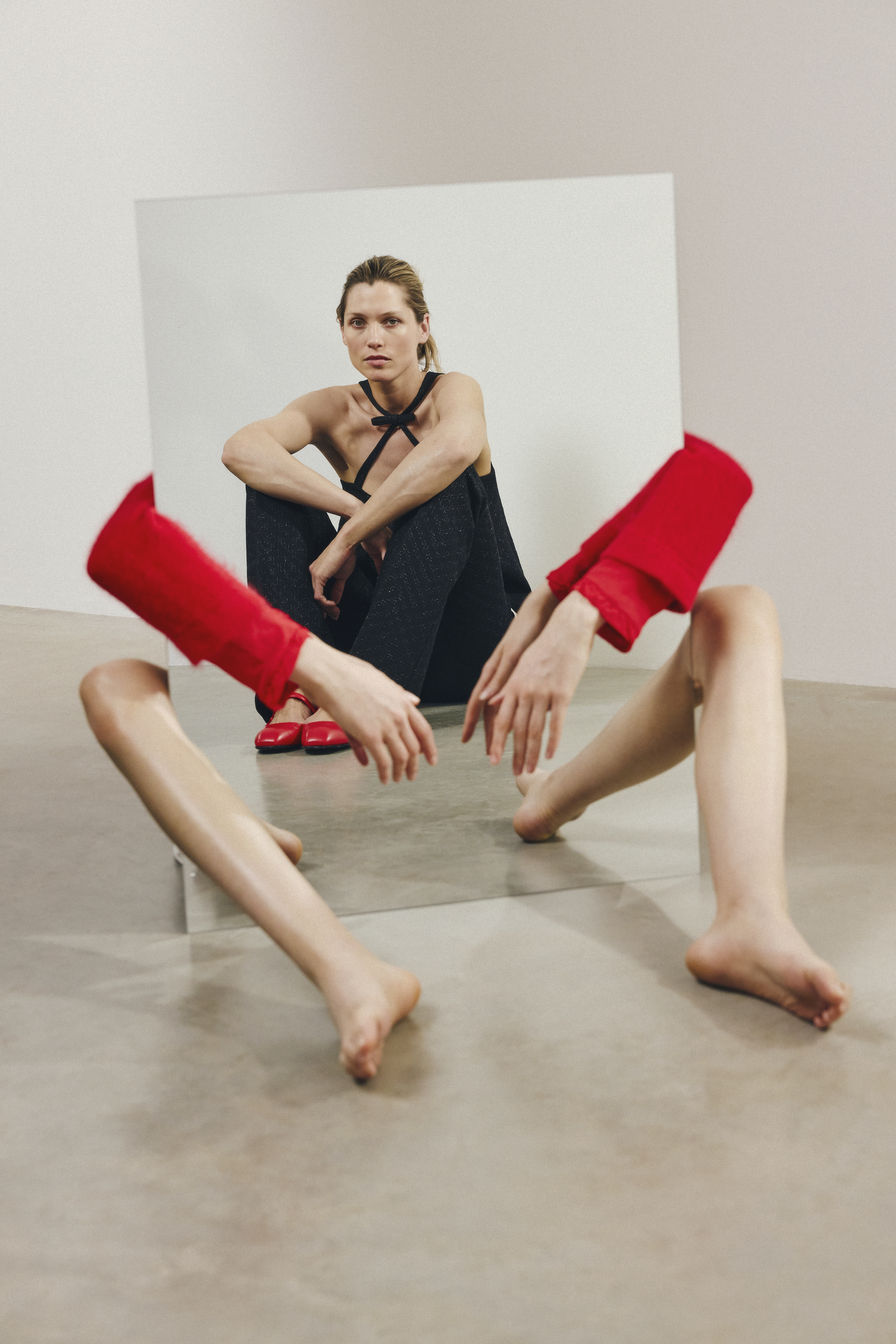 model is wearing a structured black set, a top with cross deatil and a bow and a black bootcut trousers aswell as red ballerinas