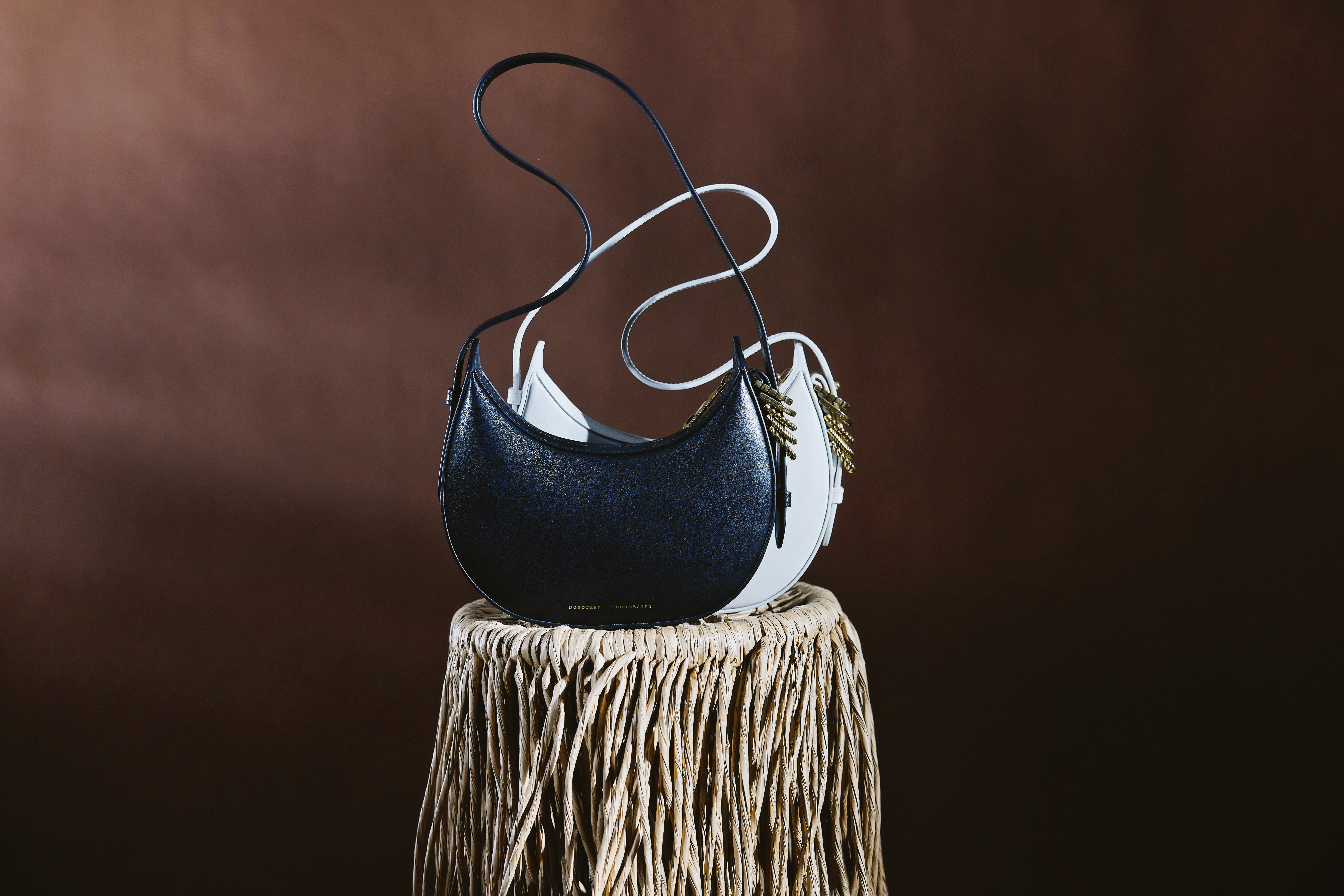two half moon leather bags in balck and white with golden details on a strawy table