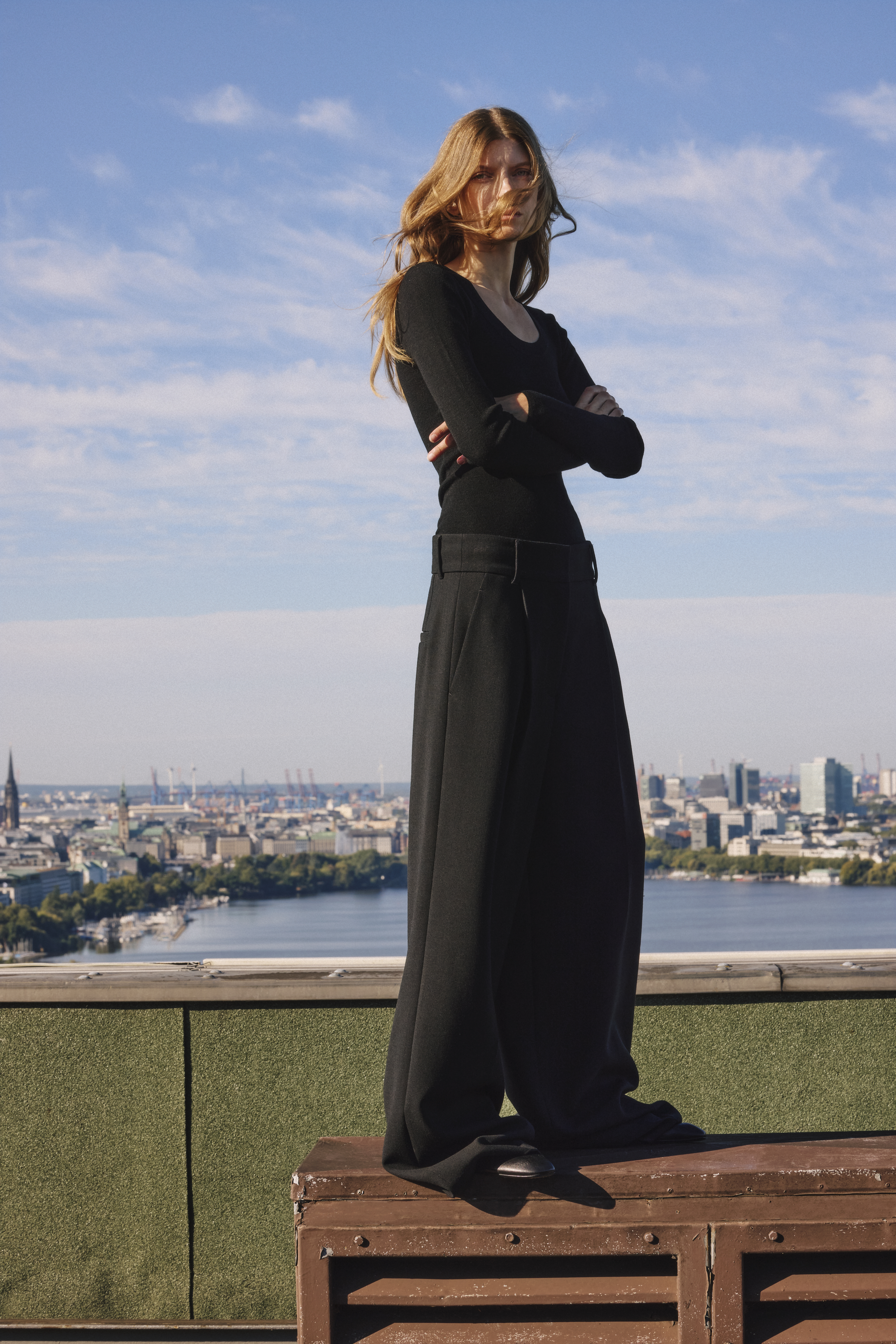 A woman with a black top and trousers standing on a bench with a skyline in the back