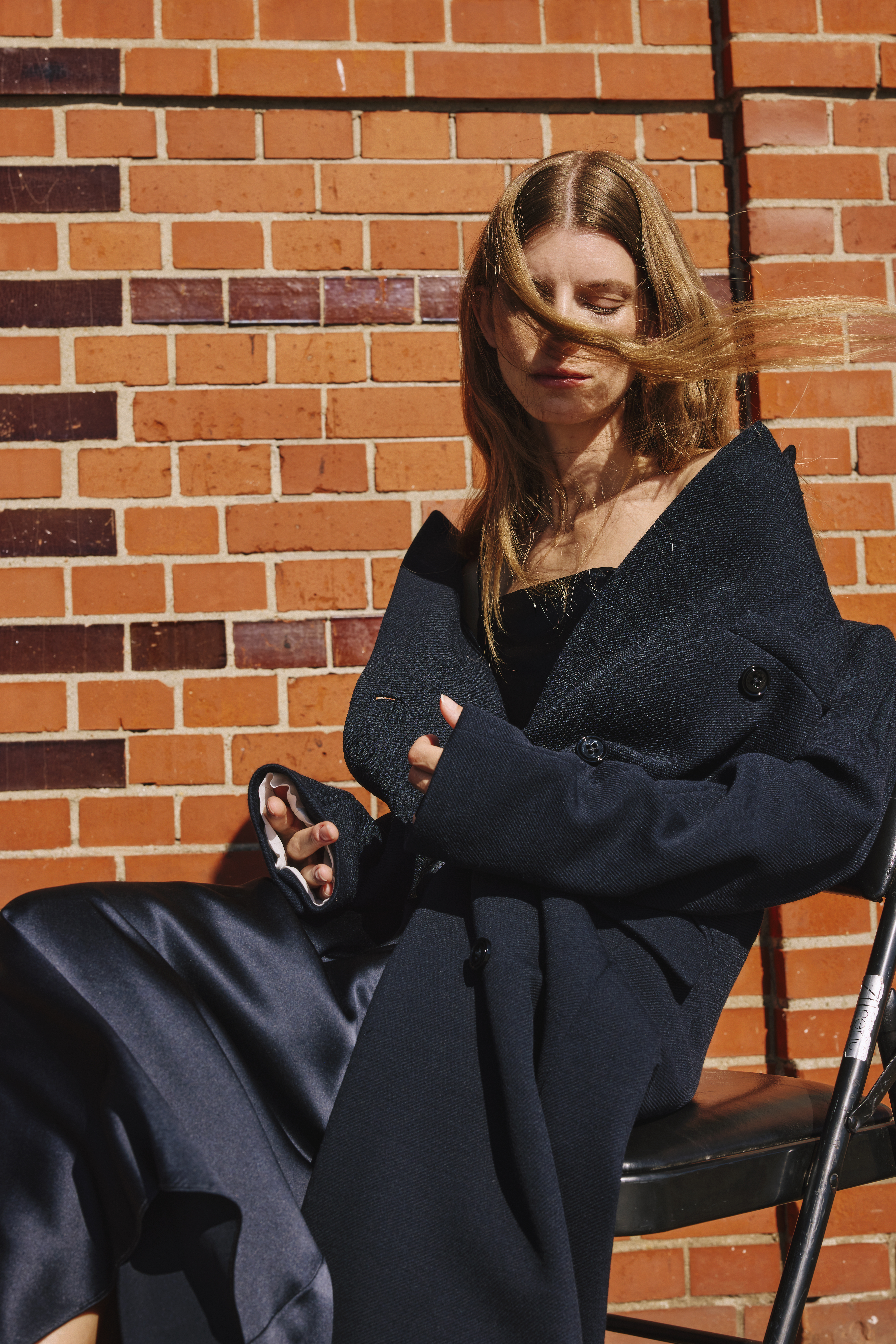 woman is sitting on a chair wearing a blue wool coat and a blue dress