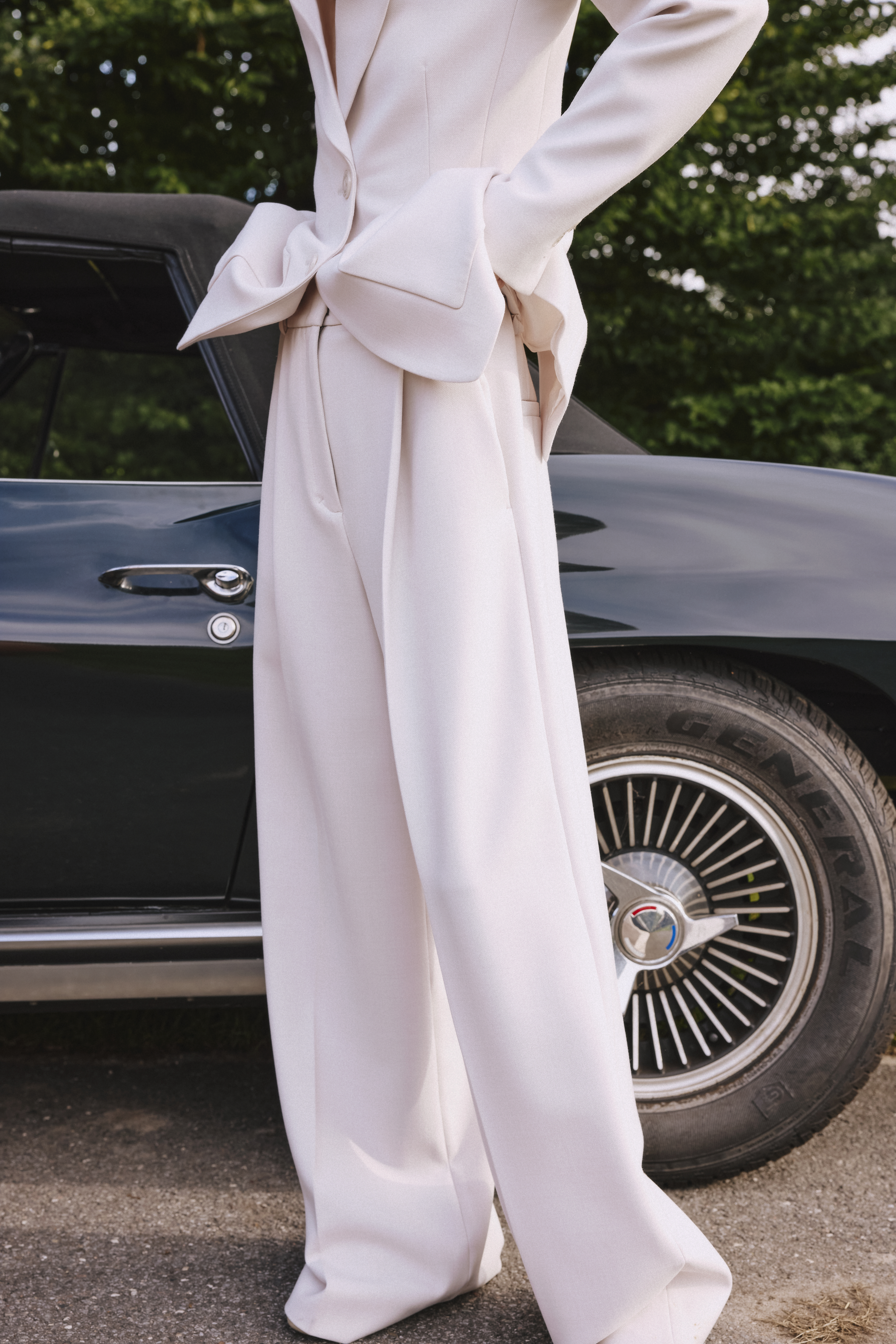 a woman is standing in front of a car wearing a white suit