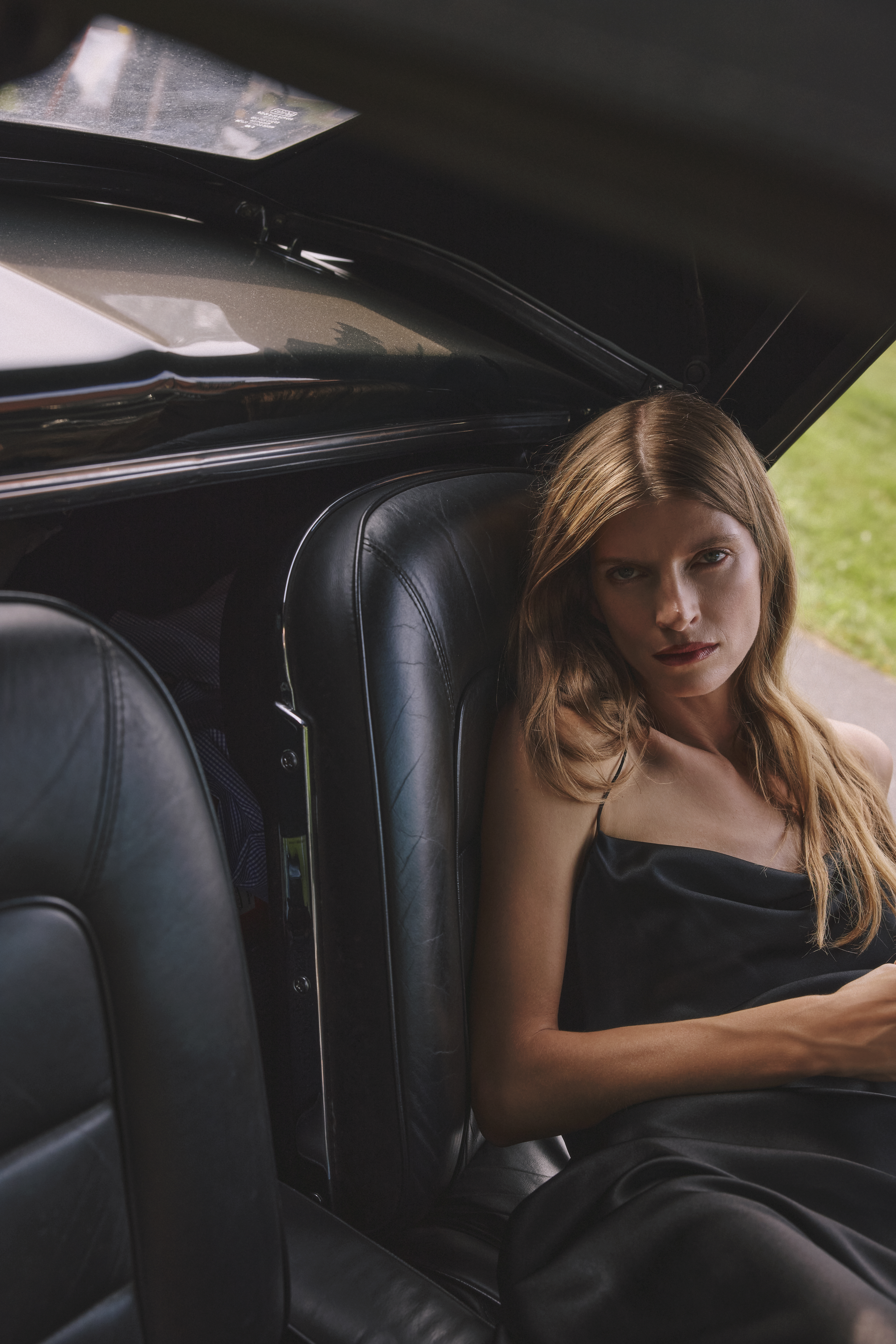 a woman is sitting in a car wearing a black satin dress