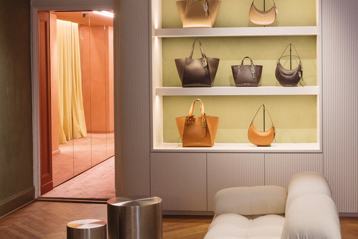 Auslage von Dorothee Schumacher Handtaschen auf beleuchteten Regalen neben einem weißen Sofa und einem Ankleidebereich im Hintergrund im Dorothee Schumacher Store.