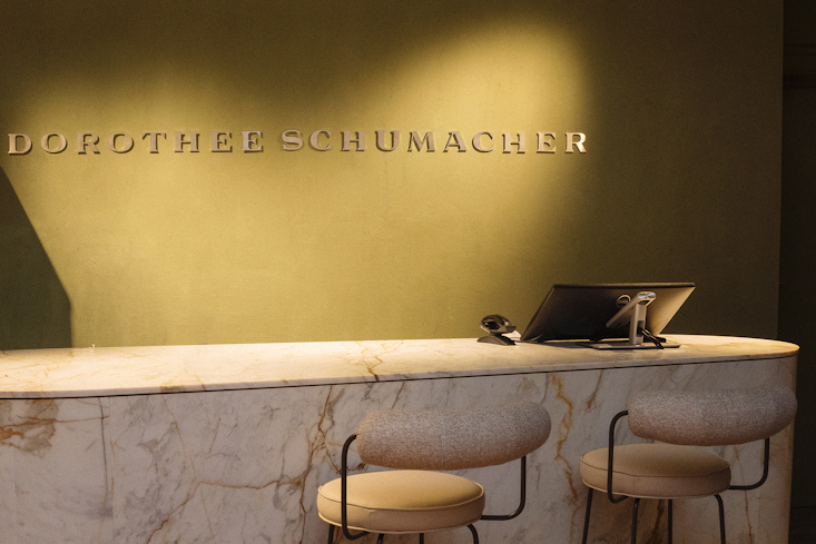 Detailansicht der Marmor-Empfangstheke im Dorothee Schumacher Geschäft mit dem beleuchteten 'DOROTHEE SCHUMACHER' Logo an der olivgrünen Wand.