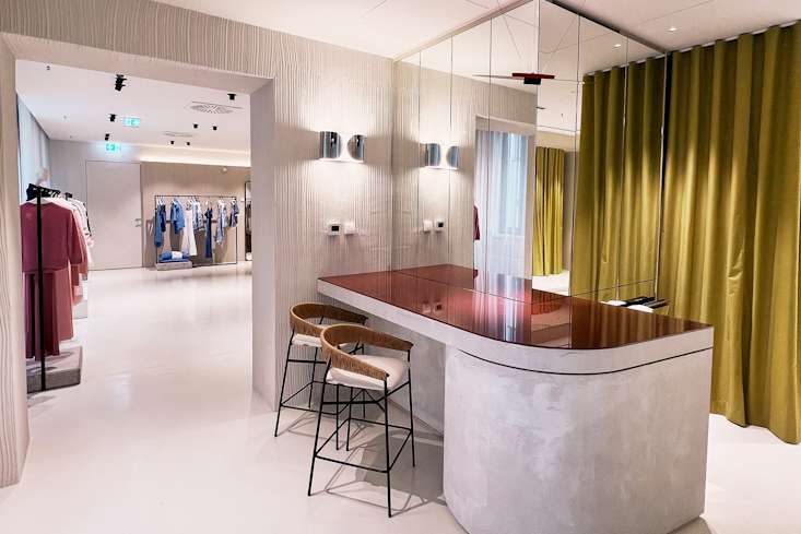 Beratungsbereich im Dorothee Schumacher Geschäft in Dresden mit einer stilvollen rotbraunen Theke, Barhockern und einem Spiegelbereich.